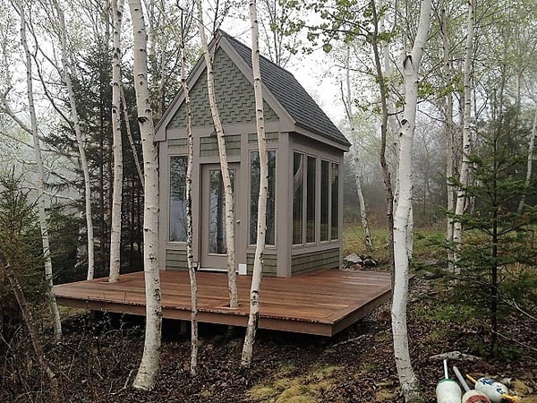 A single level Garapa wood deck around a small artist studio surrounded by birch trees in Maine