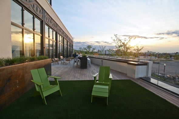 A rooftop hardwood deck with seating and bar plus articial turf and andirondack chairs above the city skyline