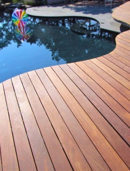 Mataverde Ipe wood pool deck with organic curves contrasts stone on a lower level, with a pool reflecting leaves and a brightly colored striped beach ball floating in the background, Mataverde Ipe wood pool deck with organic curves contrasts stone on a lower level, with a pool reflecting leaves and a brightly colored striped beach ball floating in the background,