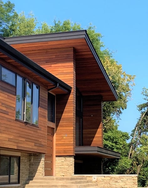 This home exterior design wraps the house, including the outside corners and soffits, with Ipe wood rainscreen system using  for a stunning facade. 