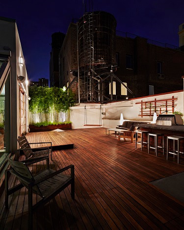Ipe rooftop deck at night under an industrial New York City skyline