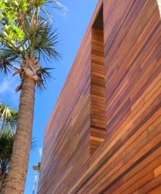 Garapa hardwood rainscreen shown installed on a Florida home, with blue sky and a palm tree next to it. Garapa wood rainscreen siding shows off its natural beauty in the Florida sun.