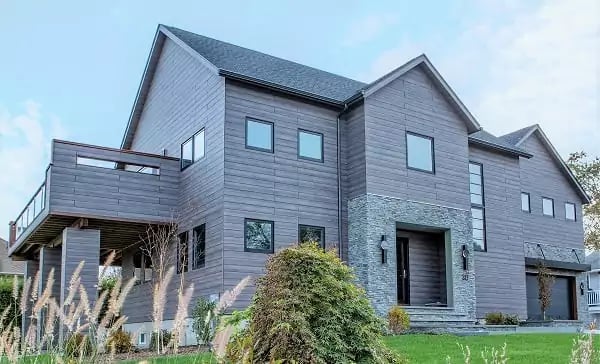 Custom home on Rhode Island coastline showcases Pura NFC Aged Ash Wood Decor  with a stone entryway and a 2nd floor deck with beach grass, shrub in the foreground.