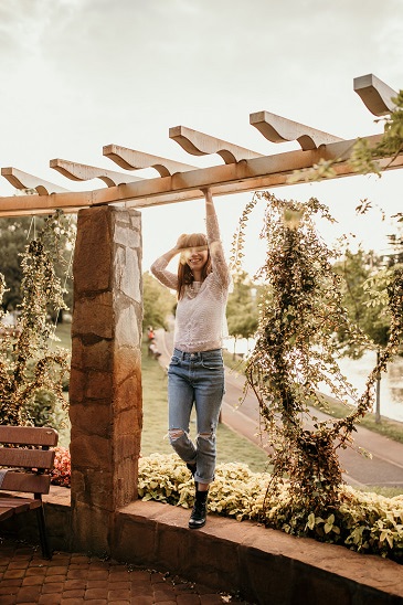 A stone and wood pergola with a young woman standing and smiling underneath.