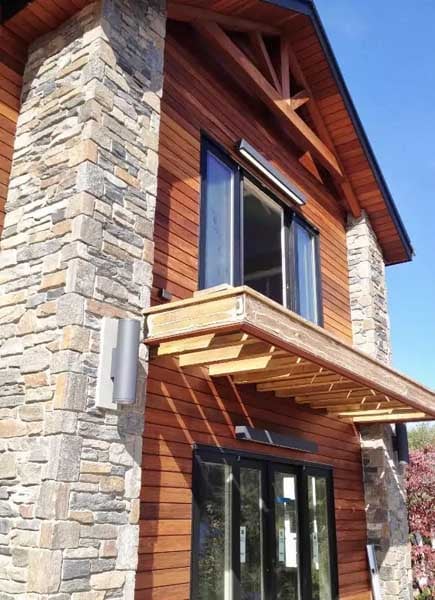 Vertical Ipe wood rainscreen siding and covered soffits contrast with stone accents